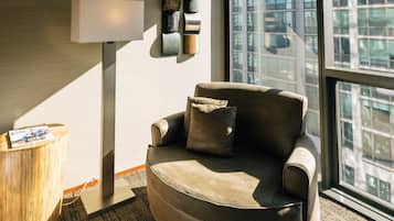 A modern living room with a leather sofa, a floor lamp, and a view of a cityscape through large windows.