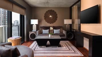 A modern living room with a sofa, coffee table, and two side tables, a large wall clock, and a flat-screen TV mounted on the wall.