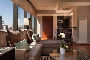 A modern living room with a sectional sofa, a glass coffee table, and a view of the city through large windows.