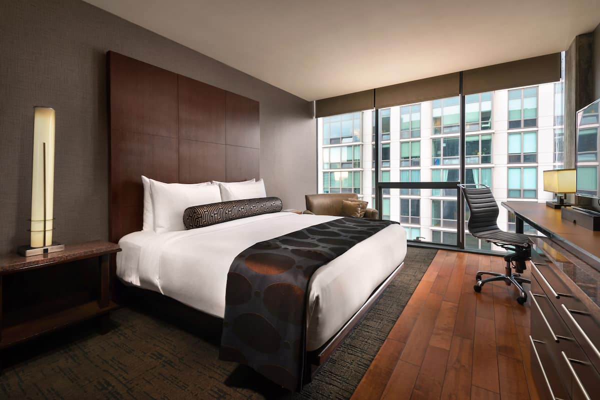 Une chambre d’hôtel moderne, dotée d’un grand lit, d’un bureau et offrant une vue sur le paysage urbain grâce à de grandes fenêtres.
