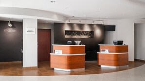 Een hotel receptie met twee houten balies, een donkere muur met een bloemenmotief, en een bordje met 'The Market' en 'Marriott Bonvoy'.