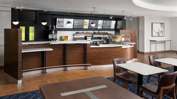 Een moderne hotellobby met een receptiebalie, een zithoek en een koffieapparaat.
