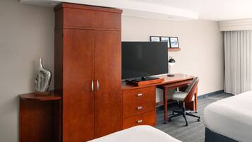 A hotel room with a wooden desk, a television, a bed, and a chair.