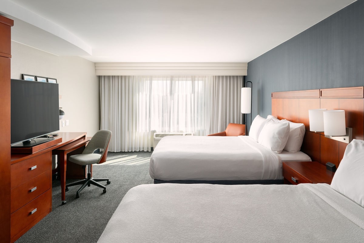 Habitación de hotel con dos camas, un escritorio, una silla y un televisor.
