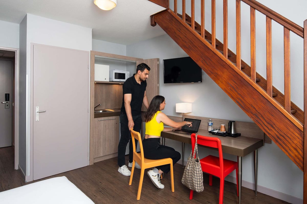 A hotel room with a wooden staircase, a desk with a laptop, a TV, and a microwave.