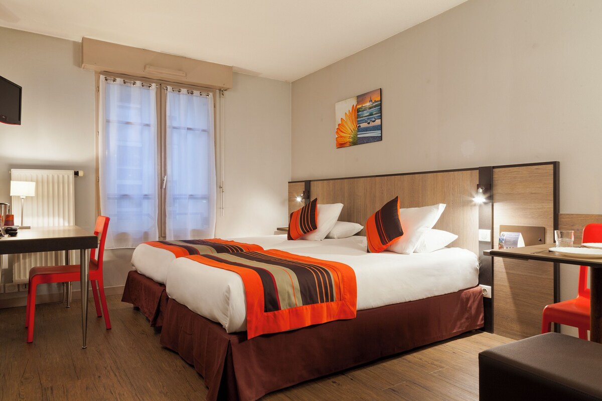 Una habitación de hotel con cama, escritorio, silla y ventana con cortinas.