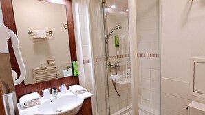 Un baño moderno con ducha envuelta en vidrio, un lavamanos con espejo y un inodoro.
