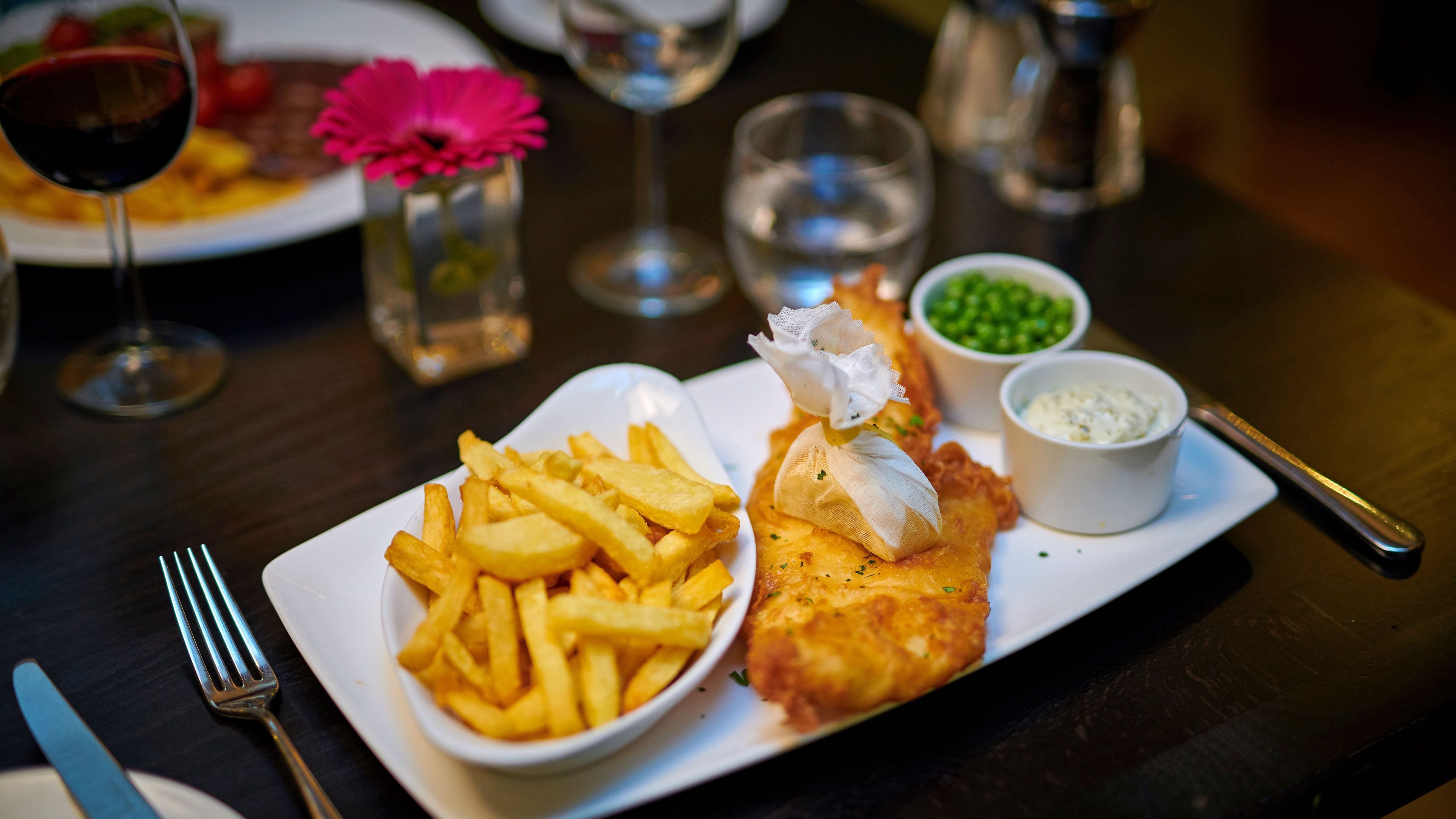 A plate of fish and chips with French fries, tartar sauce, and peas.