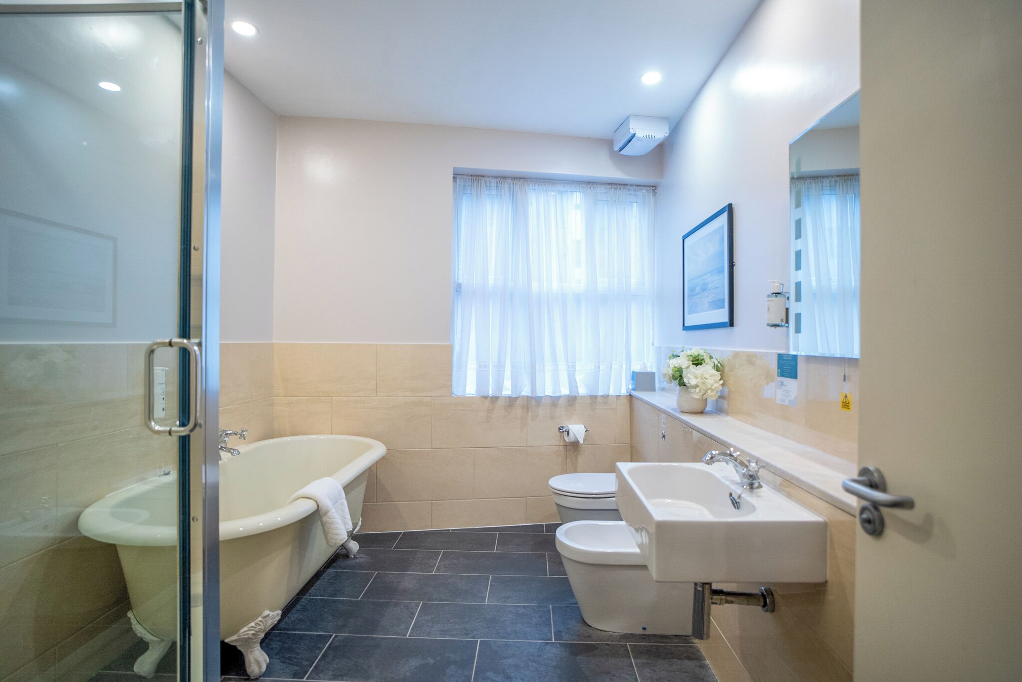 A modern bathroom with a glass shower enclosure, a freestanding bathtub, a toilet, and a sink with a mirror above.