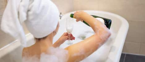 A person in a bathtub with bubbles, holding a glass and pouring champagne.