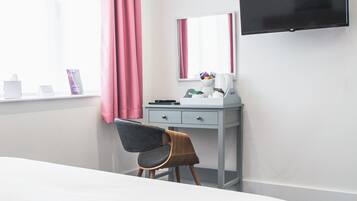 A hotel room with a bed, a desk with a chair, a flat-screen TV, and a window with curtains.
