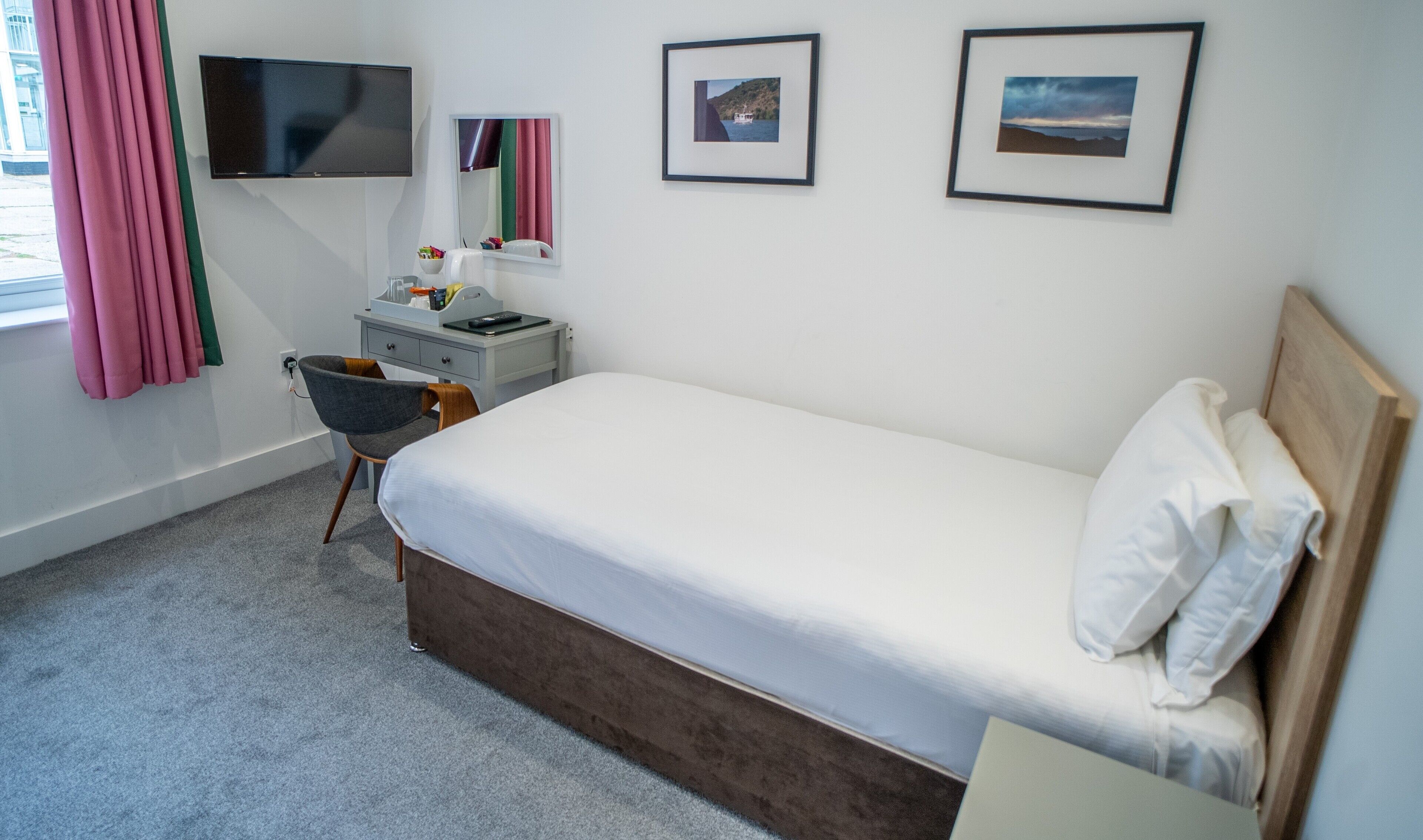Un dormitorio con cama, escritorio, silla, televisor y cuadros en la pared.