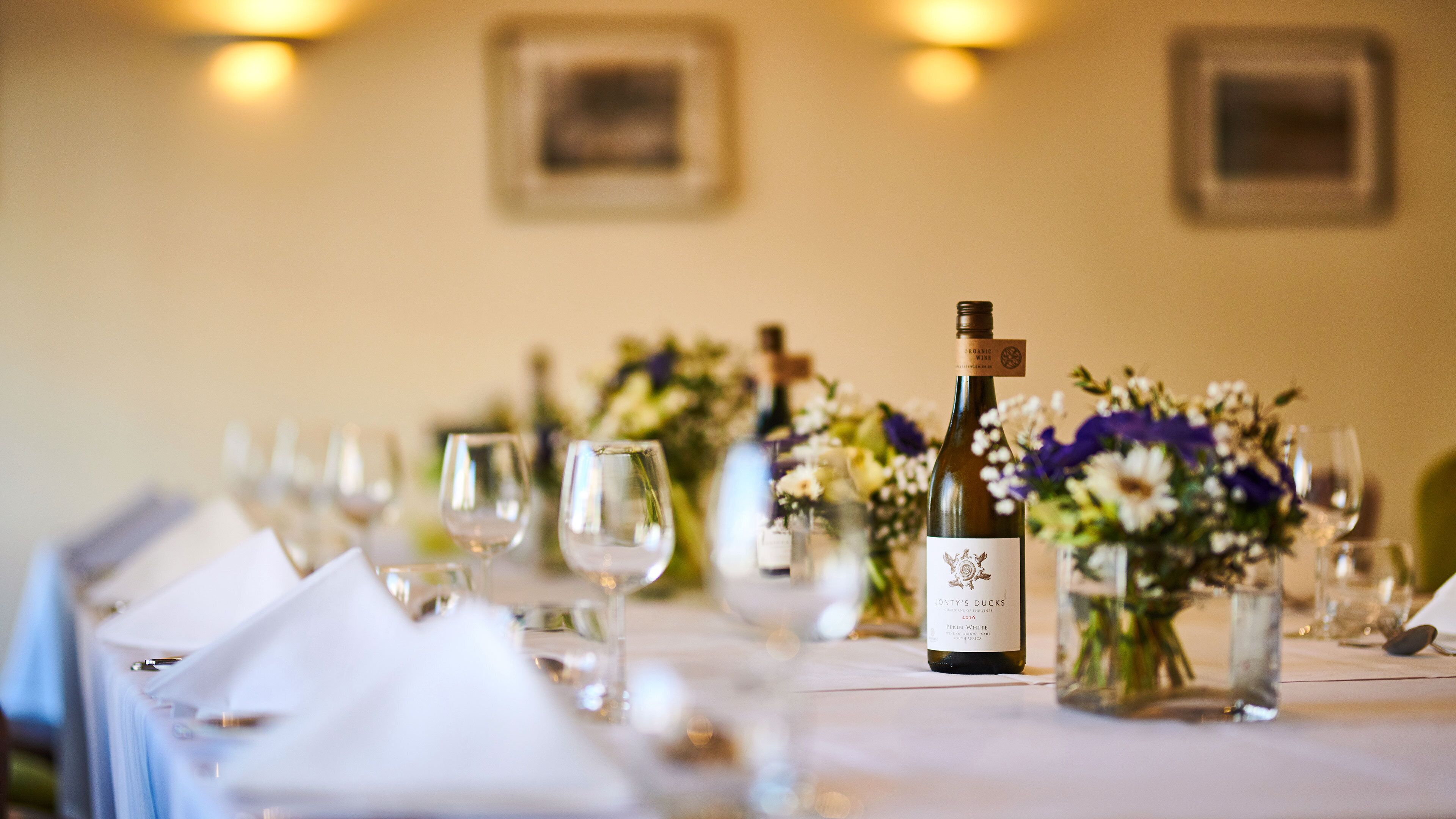 A table set for a meal with a bottle of wine, glasses, and floral centerpieces.