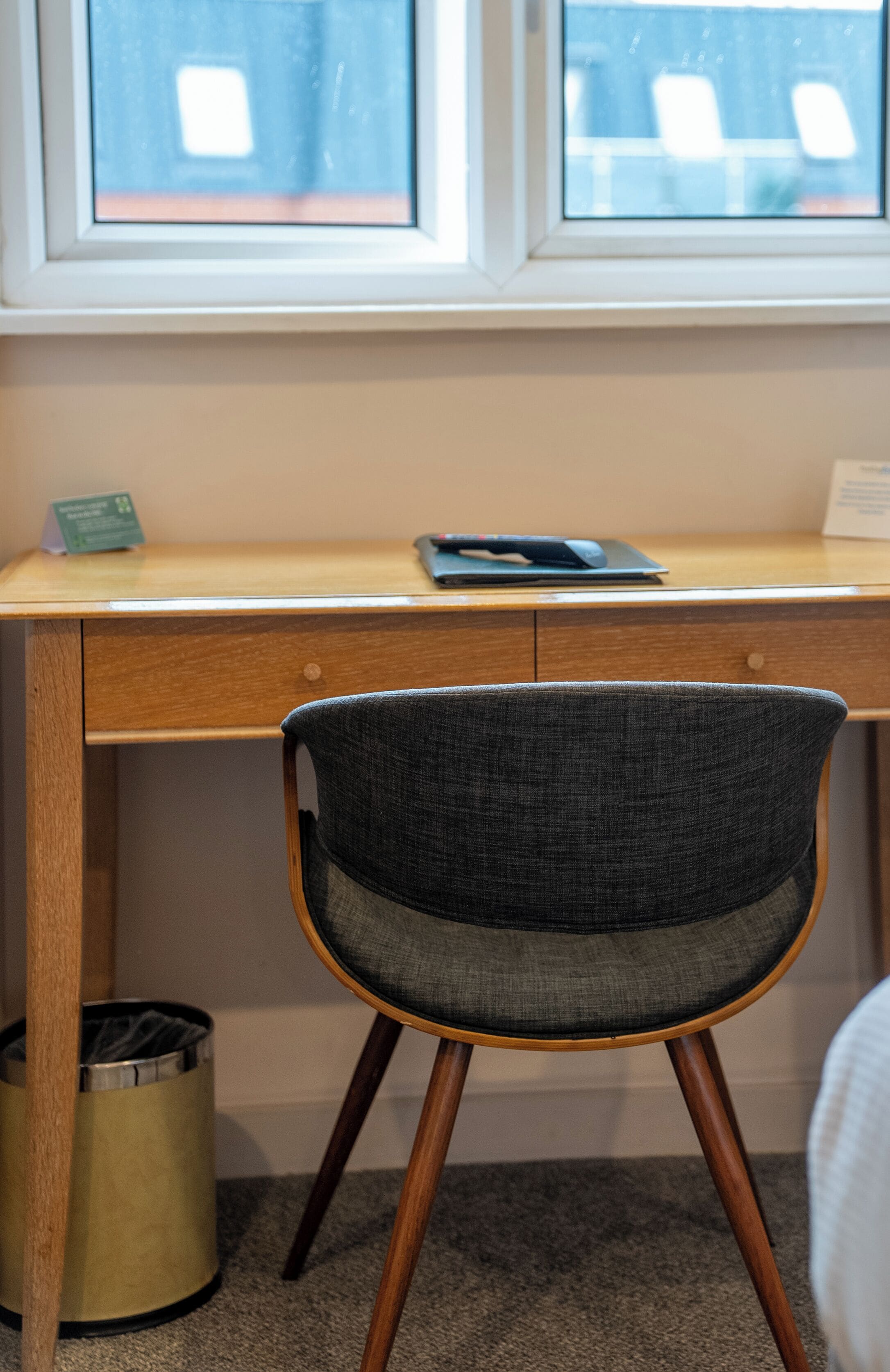 A wooden desk with a laptop and a green sign, a grey chair, and a trash can.