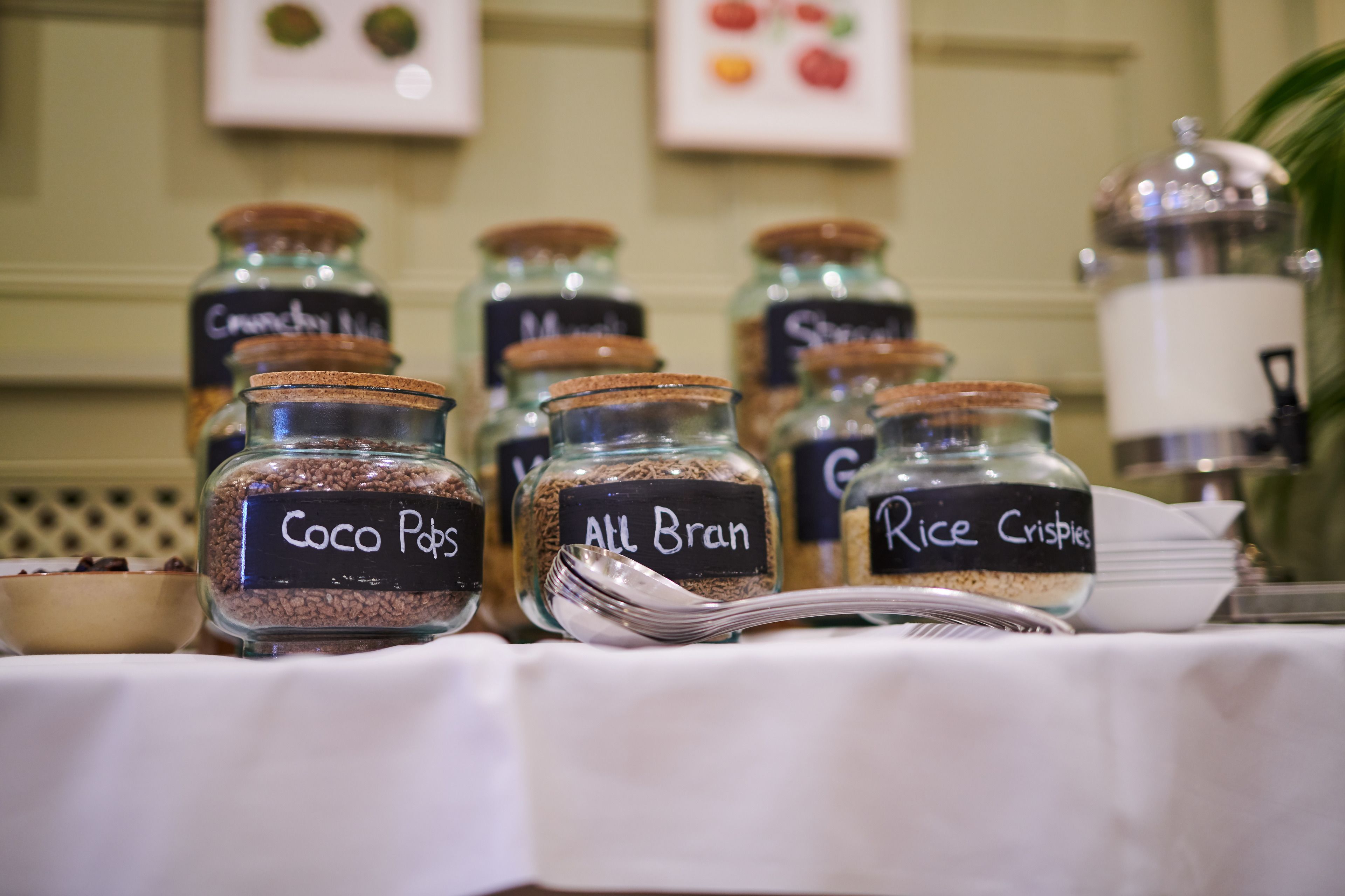 Potes de vidro etiquetados com alimentos como Coco Pops, All Bran e Rice Crisps sobre uma mesa.