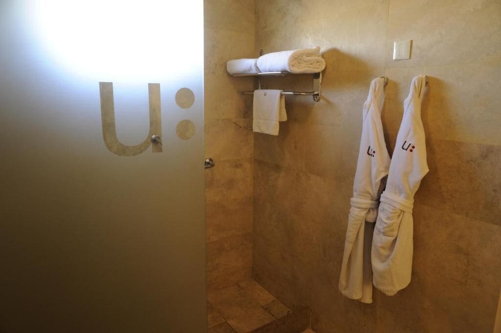 A bathroom with a shower, a towel rack with towels, and a wall-mounted light fixture.