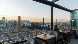 Een restaurant op een dak met uitzicht over de stad, tafels met stoelen en een vaas met bloemen.