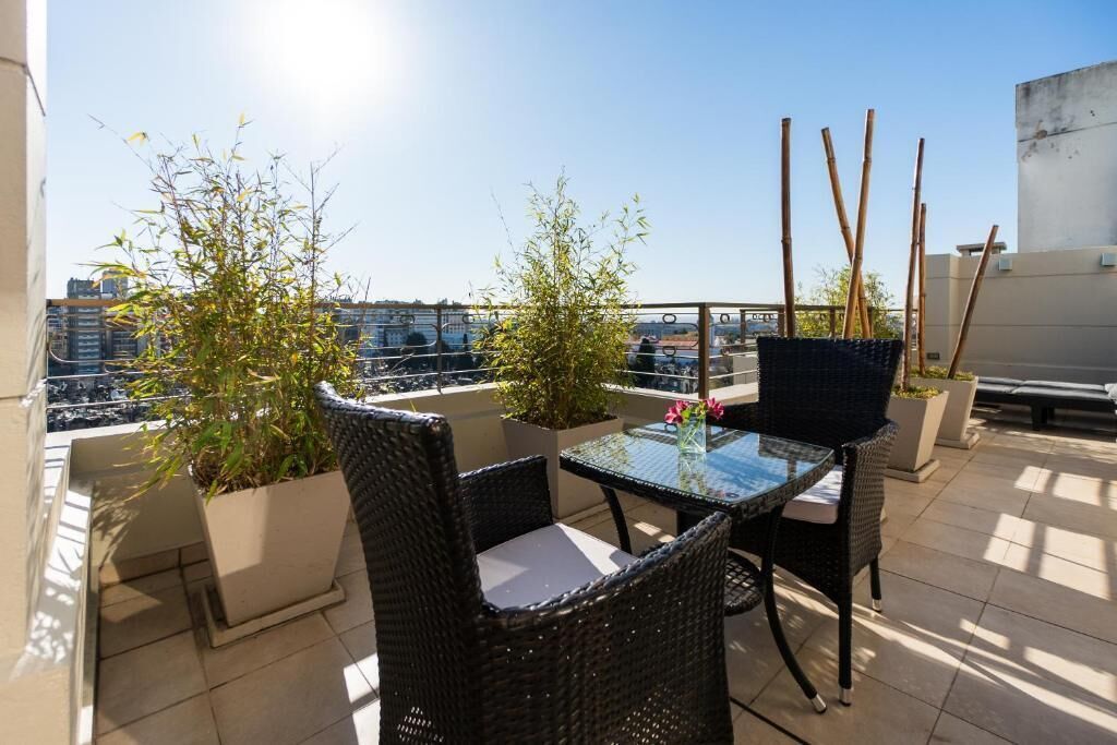 A rooftop terrace with wicker furniture, potted plants, and a clear view of the cityscape.