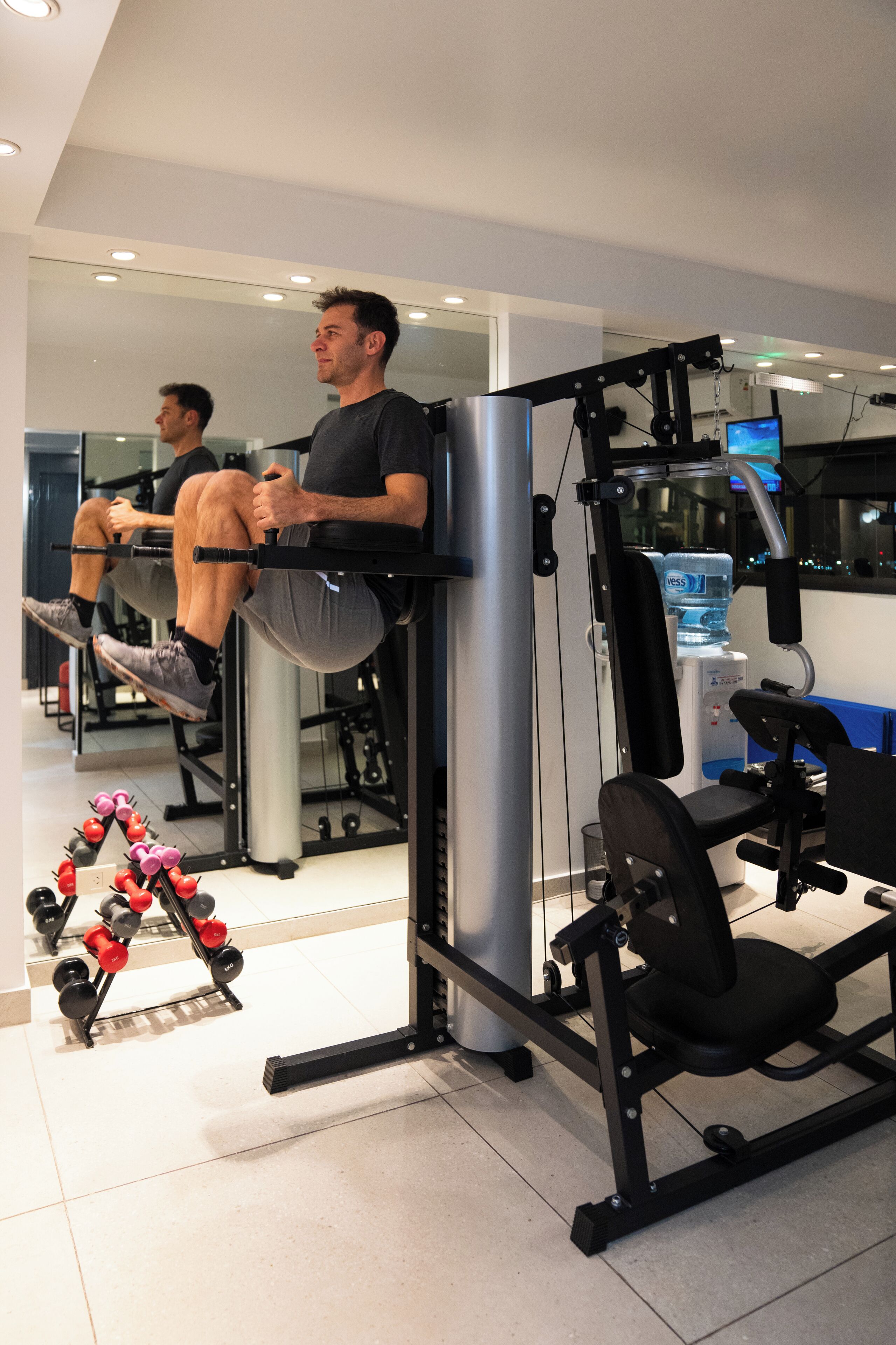 A gym with exercise equipment, a water dispenser, and a mirror reflecting the room.