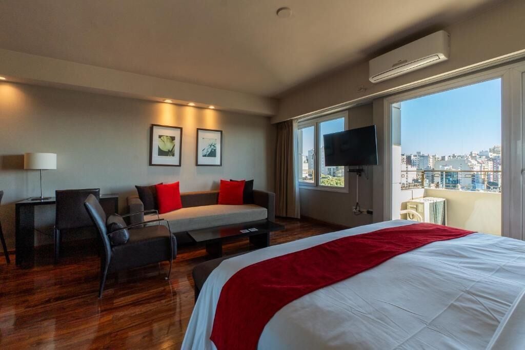 Habitación de hotel con cama, sofá, televisor, escritorio y vista a la ciudad.