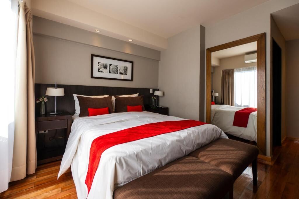 A hotel room with a large bed, bedside tables, a mirror, and a framed picture on the wall.