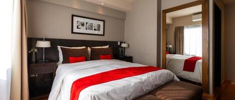 A hotel room with a large bed, bedside tables, a mirror, and a framed picture on the wall.