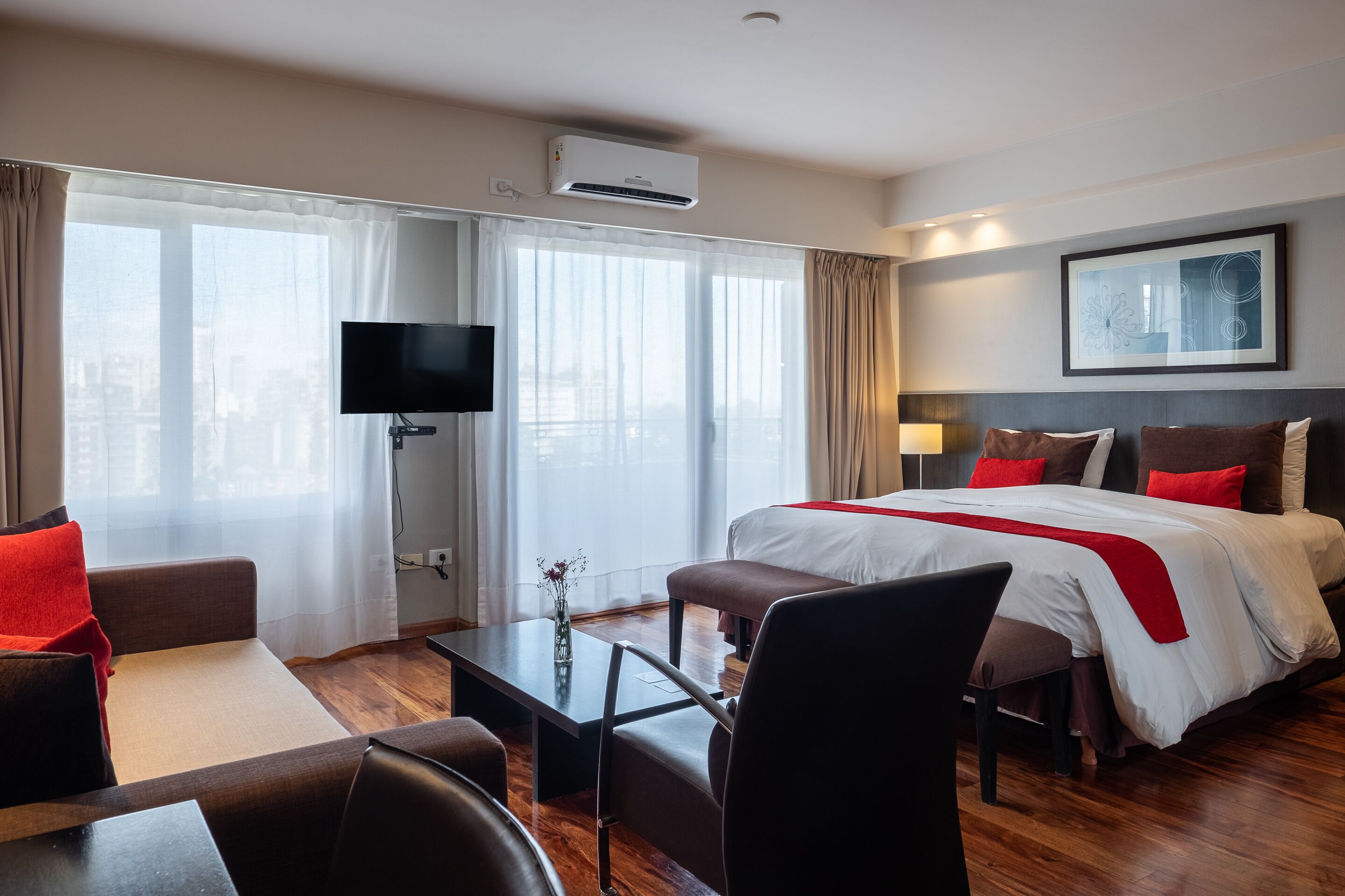 A hotel room with a bed, a desk, a chair, a TV, and a window with curtains.