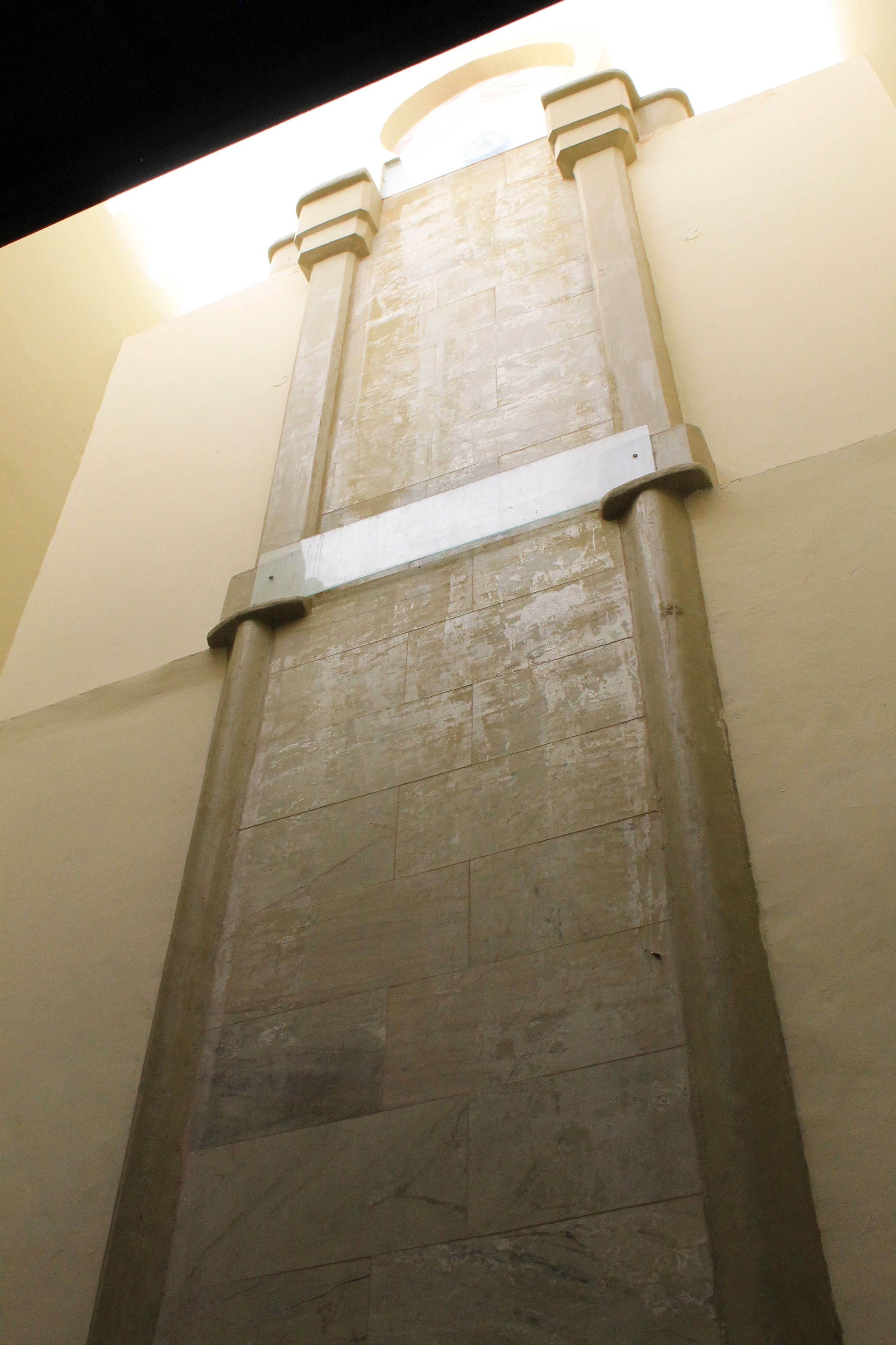 Un mur de pierre, haut et étroit, surmonté d’une console métallique.