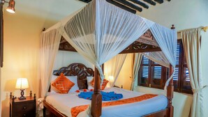 Una cama con dosel sobre cuatro columnas, cabecera de madera, ropa de cama blanca y detalles en naranja.