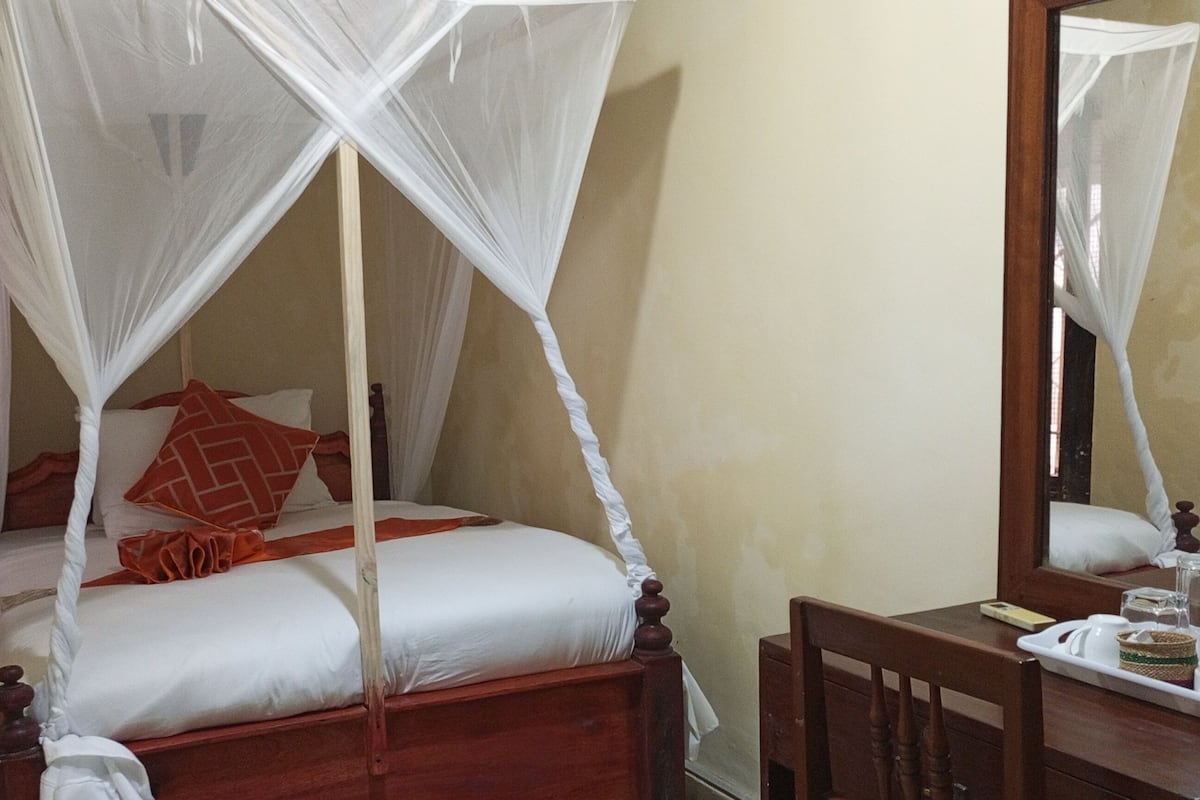 Ein Bett mit Baldachin, ein Nachttisch mit Tablett und ein Spiegel, der das Bett widerspiegelt.