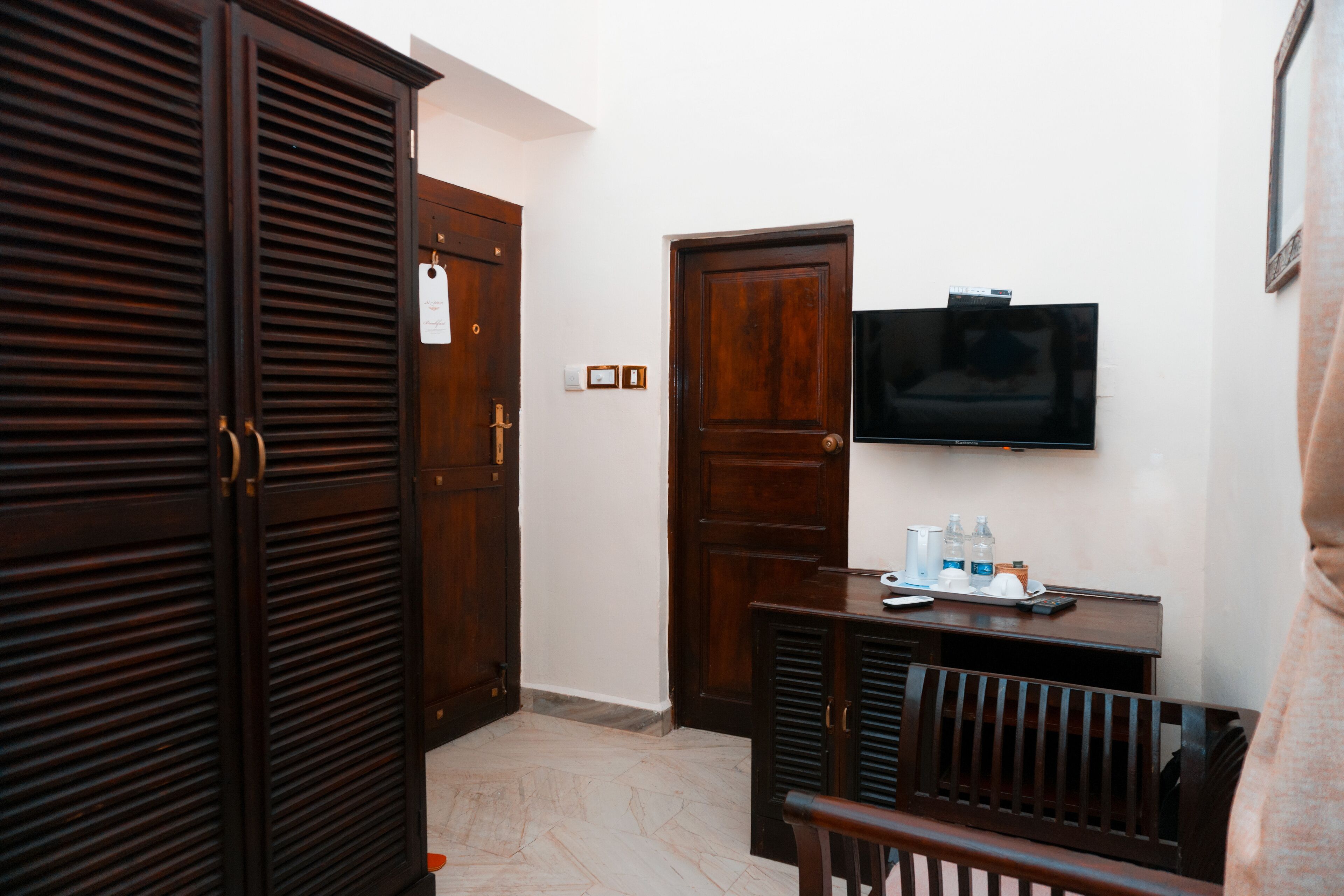 Habitación de hotel con puerta de madera, televisor montado en la pared y una mesita con artículos de aseo.