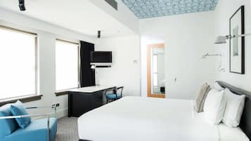A modern hotel room with a large bed, a desk with a chair, a TV, and a shower area.
