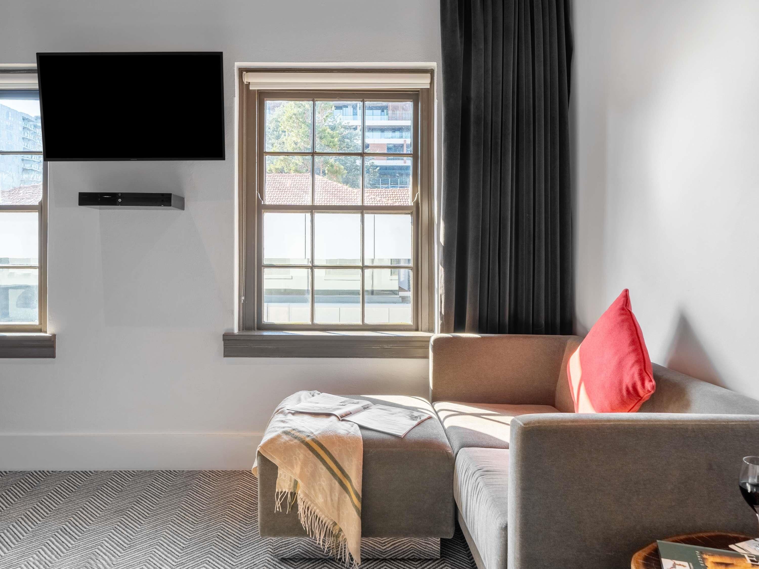Un salon moderne avec un canapé, un téléviseur fixé au mur et une fenêtre donnant sur des immeubles.