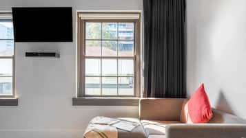 Un salon moderne avec un canapé, un téléviseur fixé au mur et une fenêtre donnant sur des immeubles.