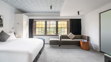 Una camera d'albergo con un letto, un divano, una finestra vista alberi e un soffitto con motivo floreale.