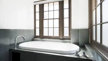 A modern bathroom with a freestanding bathtub, a window with blinds, and a stainless steel sink.