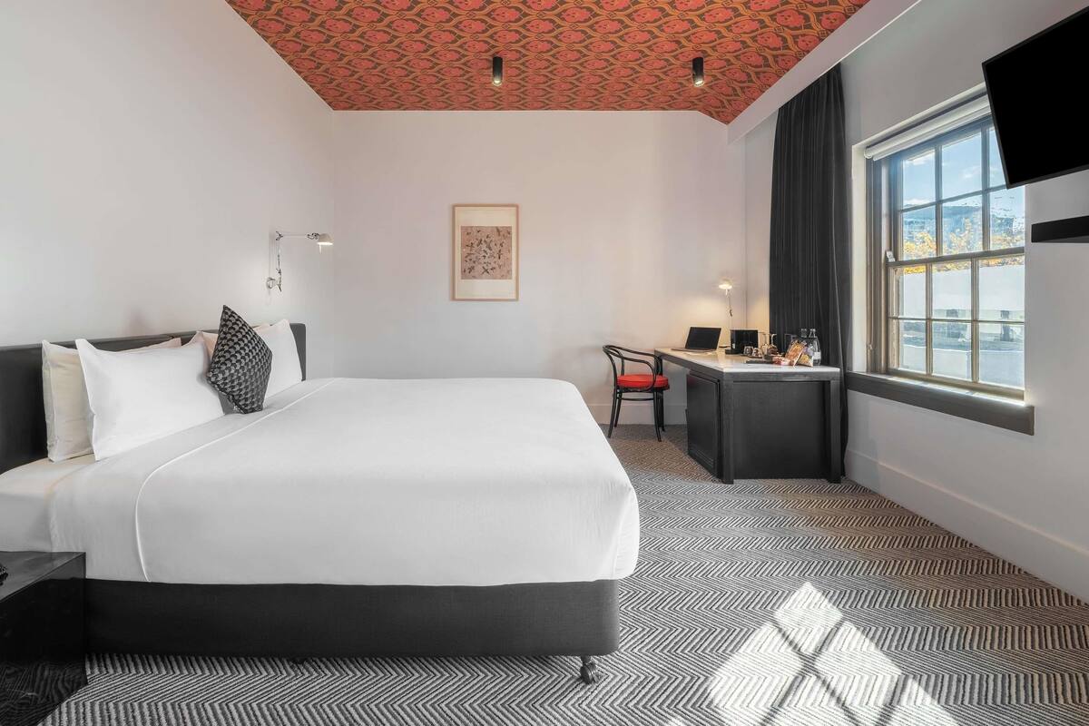 A hotel room with a bed, desk, chair, and a window with a view.