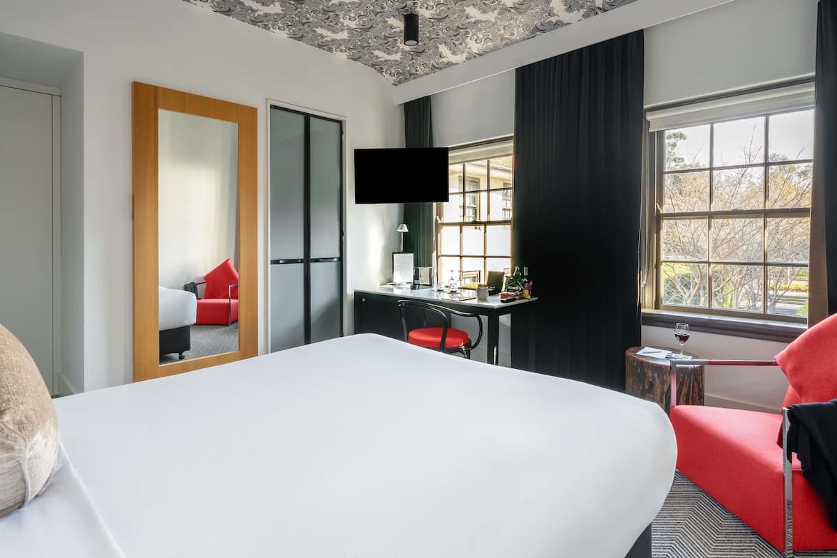 A hotel room with a bed, a desk, a chair, a TV, a window with a view, and a mirror.