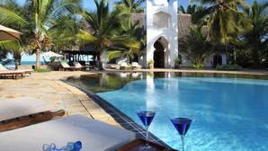 A pool area with lounge chairs, a white archway, palm trees, and a clear blue sky. - Sultan Sands Island Resort & Spa (Kiwengwa)
