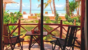A wooden deck with two chairs and a table, overlooking a beach with palm trees and the ocean. - Sultan Sands Island Resort & Spa (Kiwengwa)