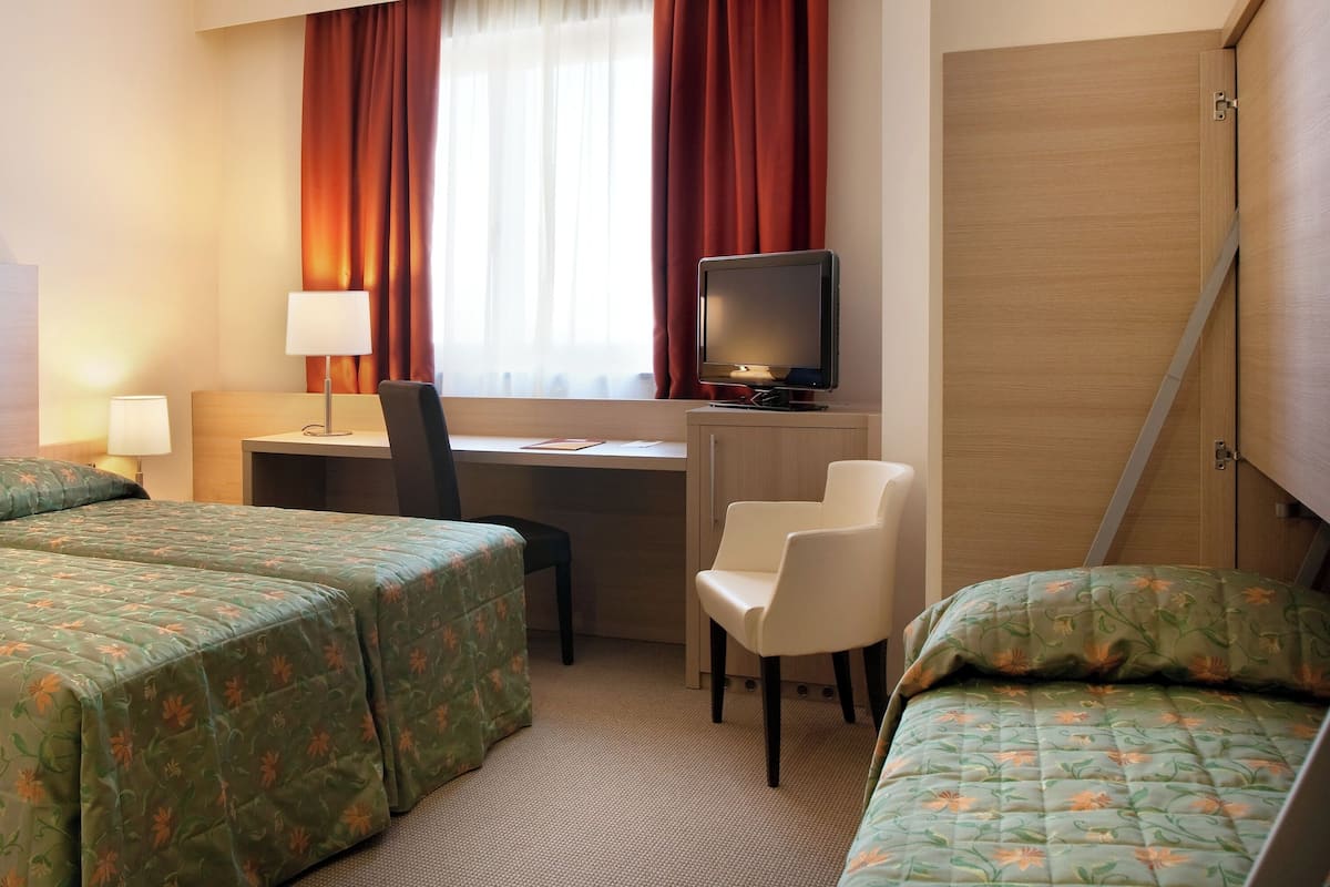 Hotellihuone, jossa on kaksi sänkyä, työpöytä, tietokone, tuoli ja televisio.