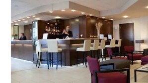 A modern lobby with a reception desk, bar area, seating with red and black sofas, and a large abstract painting on the wall.