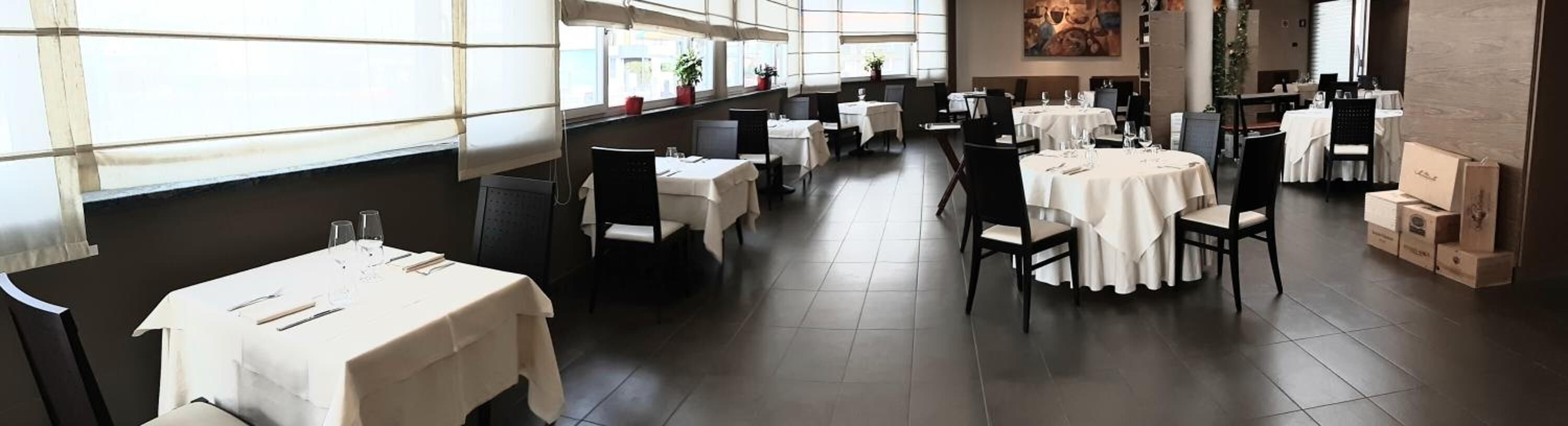 A restaurant with multiple tables and chairs, large windows, and a tiled floor.