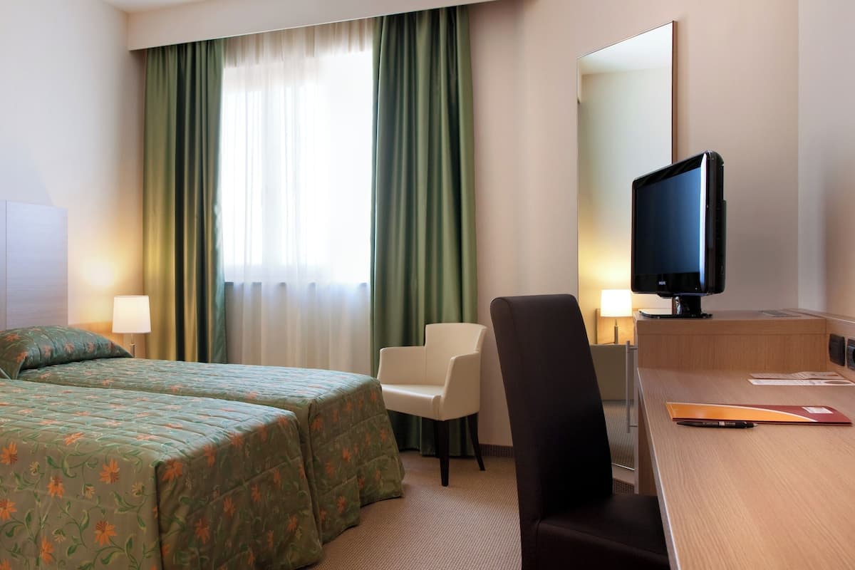 Hotellihuone, jossa on kaksi sänkyä, työpöytä, tuoli, televisio ja suuri peili.