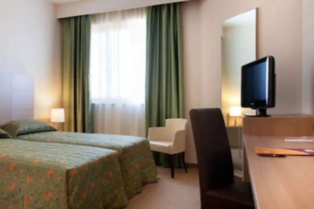 Hotellihuone, jossa on sänky, työpöytä, tuoli, televisio ja verhot.