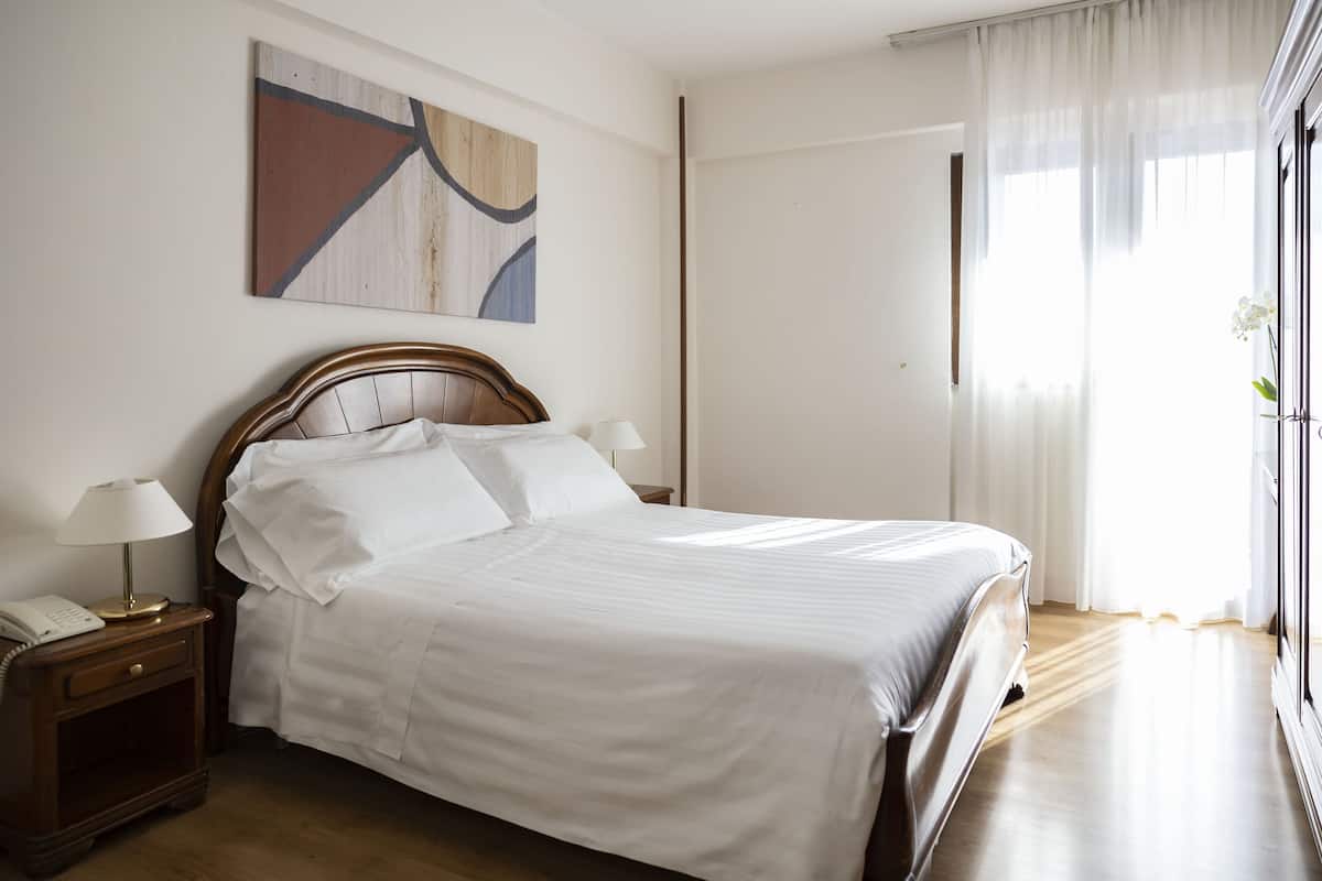 A neatly made bed with white linens, a wooden headboard, and two bedside lamps.