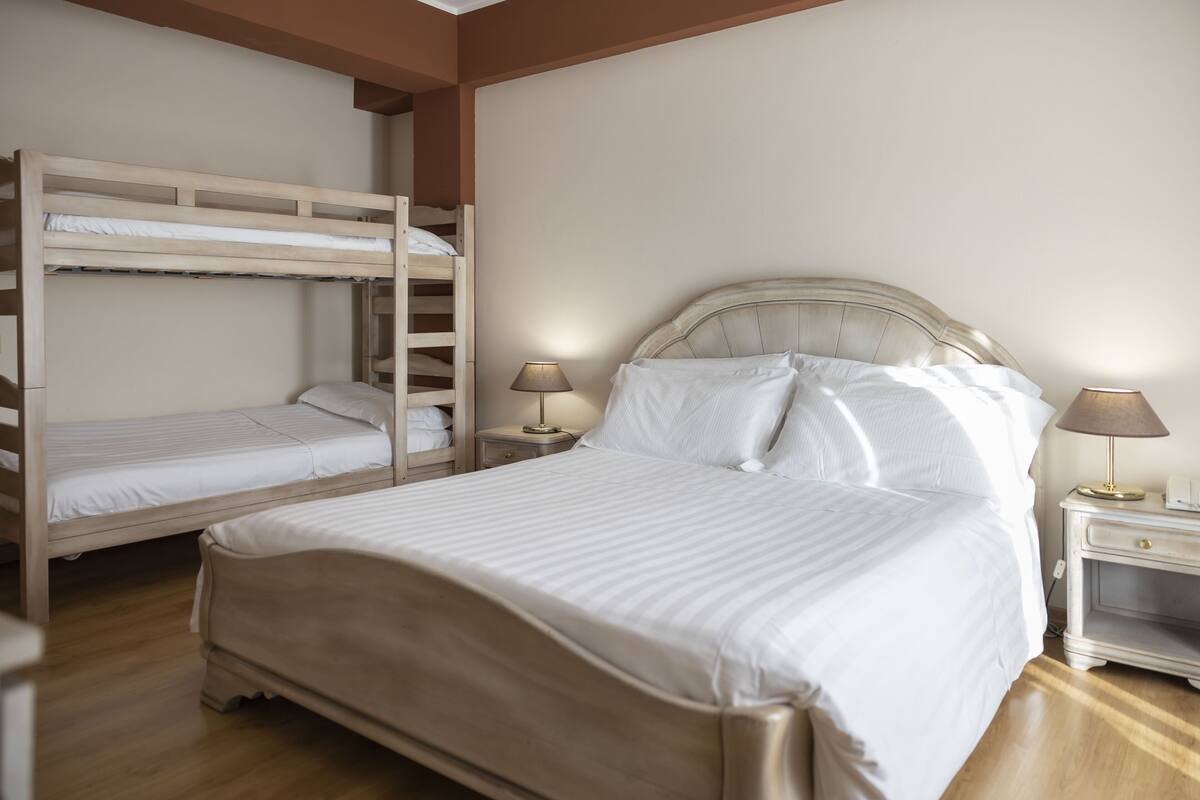 A bedroom with a large bed, a smaller bed, and a bunk bed. There are two bedside tables with lamps.