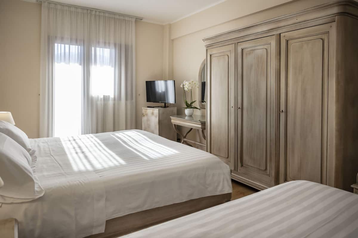 A hotel room with two beds, a TV, a desk with a lamp, and a wardrobe.