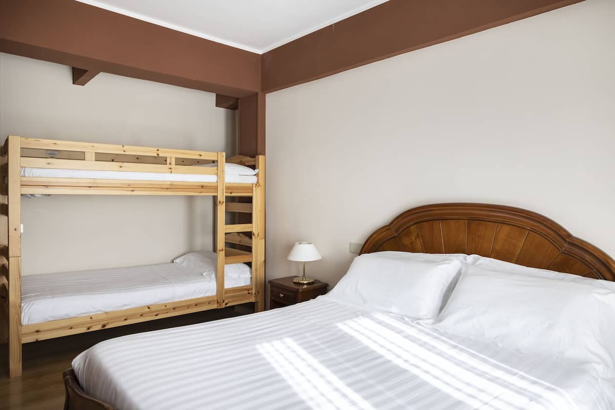 A room with a bunk bed, a single bed, and a nightstand with a lamp.