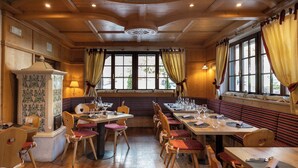 Un restaurante con interior de madera, varias mesas y sillas, y amplias ventanas con cortinas.